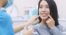 Woman in dental chair pointing to smile
