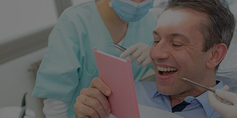 Man in dental chair looking at smile in mirror